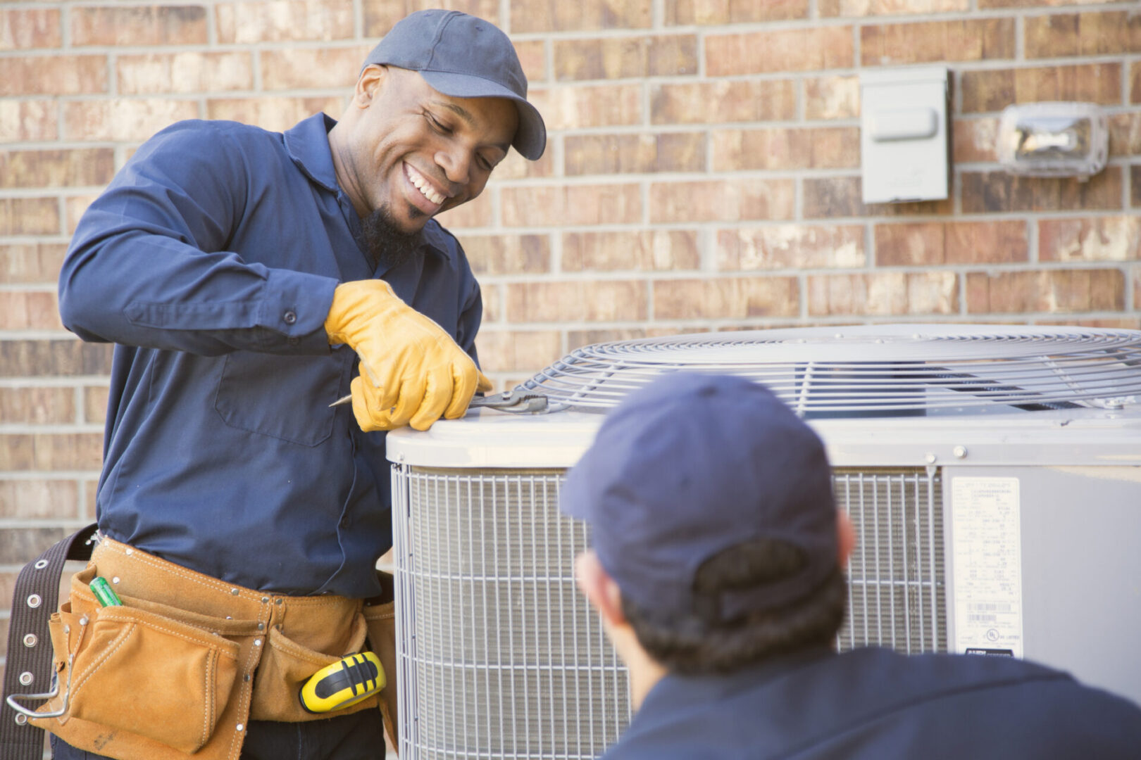 Multi-ethnic team of blue collar air conditioner repairmen at work.  They prepare to begin work by gathering appropriate tools from their tool box.