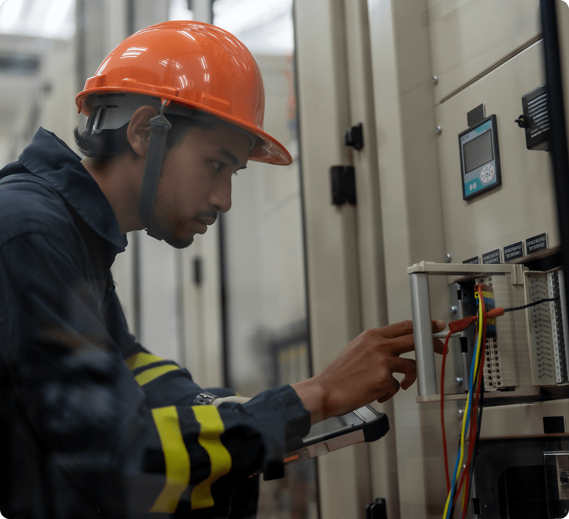 Technician working on electrical panel wearing helmet.
